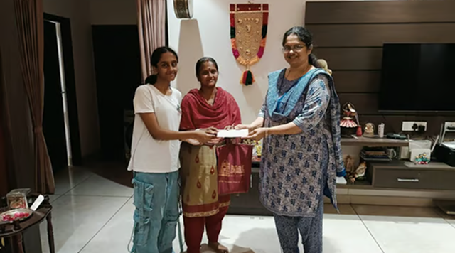 three indian women handing over a cheque in a living room
